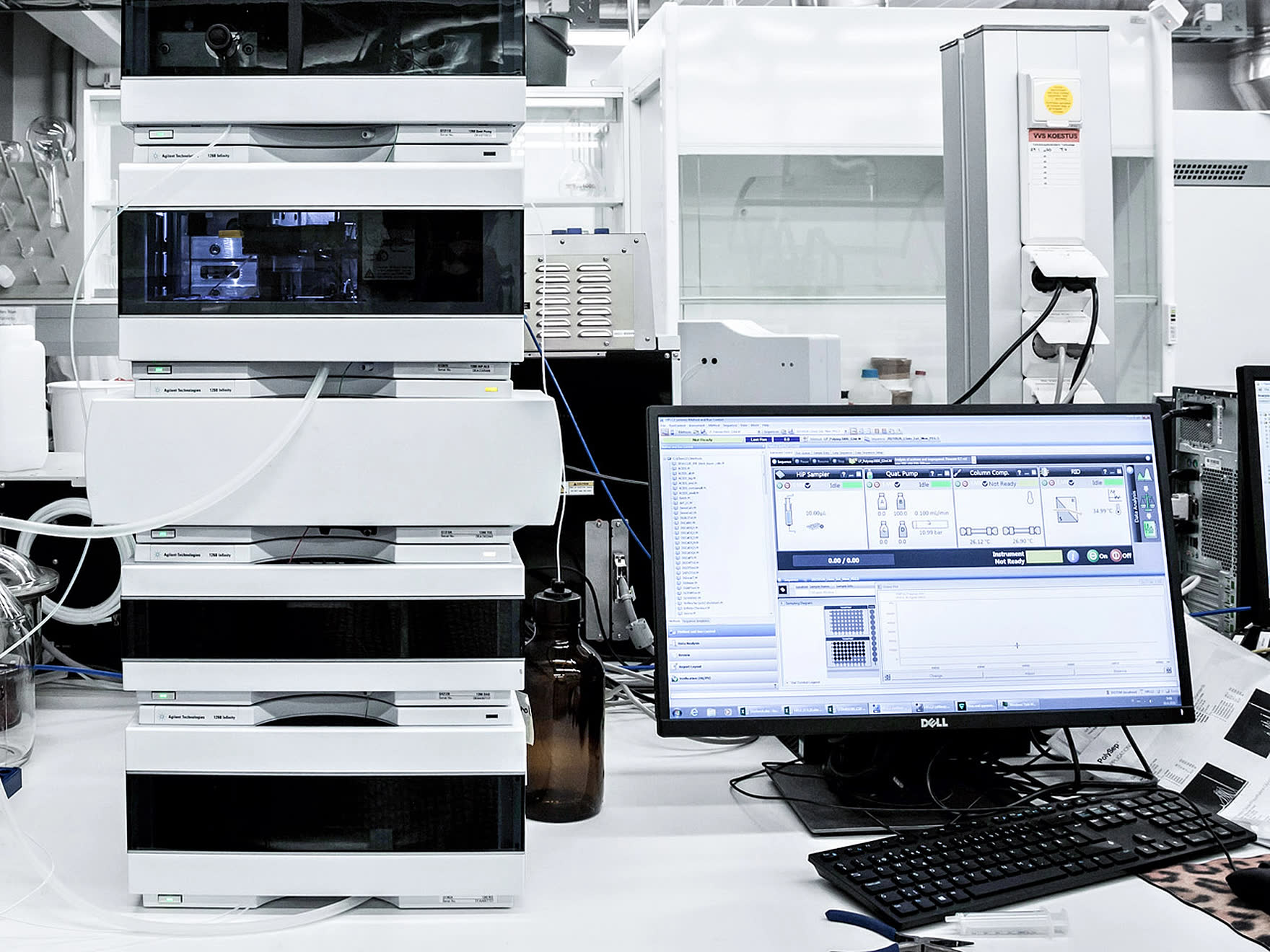 Working laboratory bench: a stacked liquid chromatography system
                  beside a monitor running the chromatography data system, with a
                  sample table and plate map on screen.